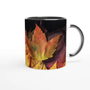 Ceramic mug with black interior featuring green, red, and yellow autumn leaves artwork
