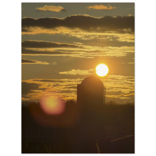 Farm silo at sunset with golden clouds and sun above horizon