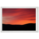 Framed landscape art print of a glowing sunset sky above dark mountain ridges, set in a matte white wood grain frame