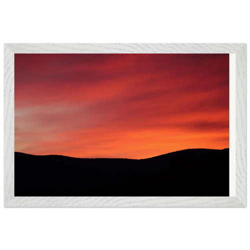 Framed landscape art print of a glowing sunset sky above dark mountain ridges, set in a matte white wood grain frame