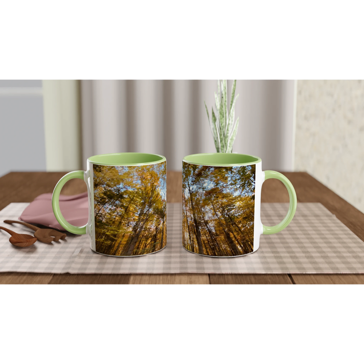 Two ceramic mugs with green handles and sunlit forest design set on a dining table