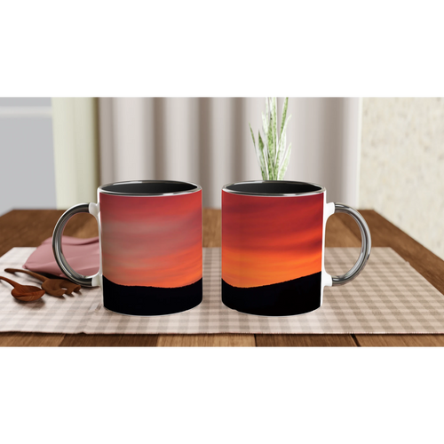 two ceramic mugs with mountain sunrise artwork on a dining table